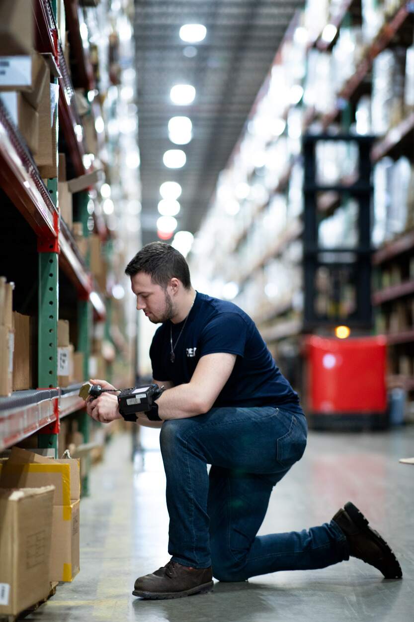 DSV medarbeider står bøyd ved lagerreol og registrerer varer